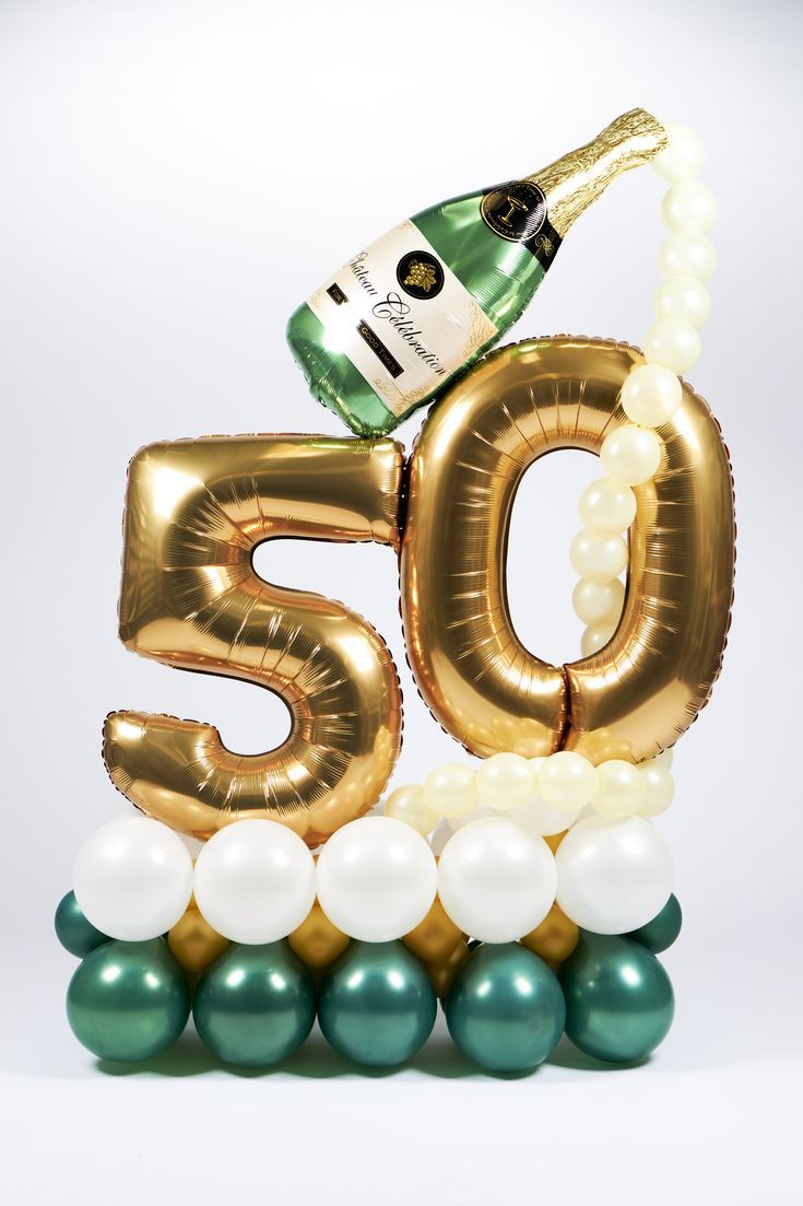 Gold number '50' balloon with green and white balloons and a bottle of champagne on a white background