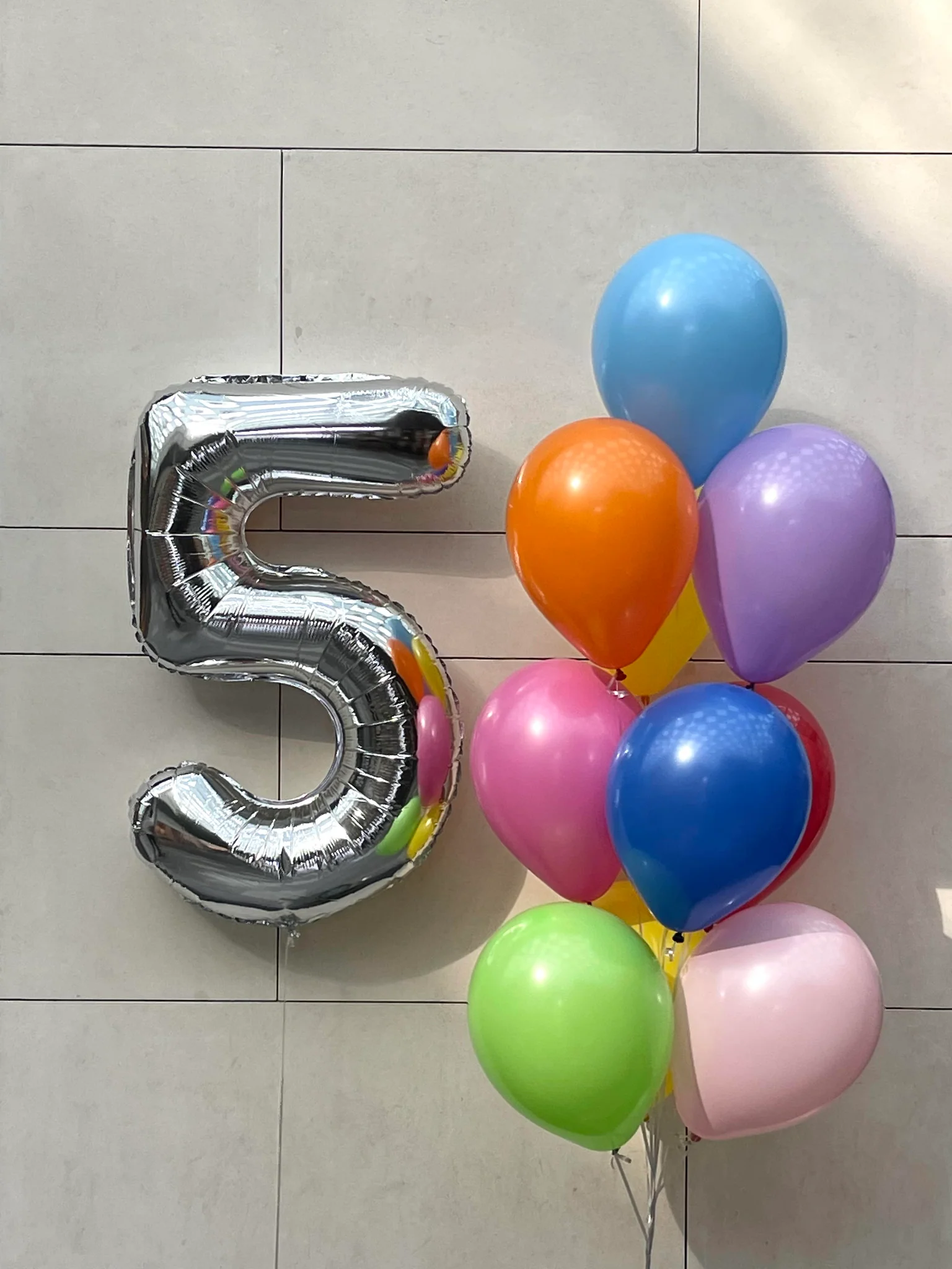 Silver number 5 balloon and colorful balloons on a tiled floor