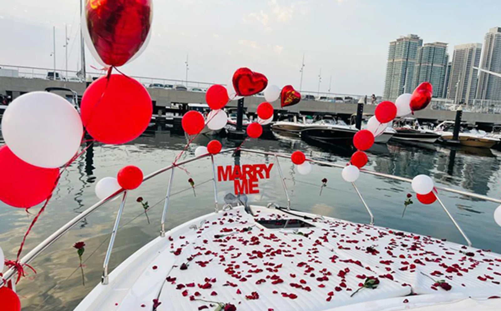 Decorated boat with balloons and 'Marry Me' sign at a marina.