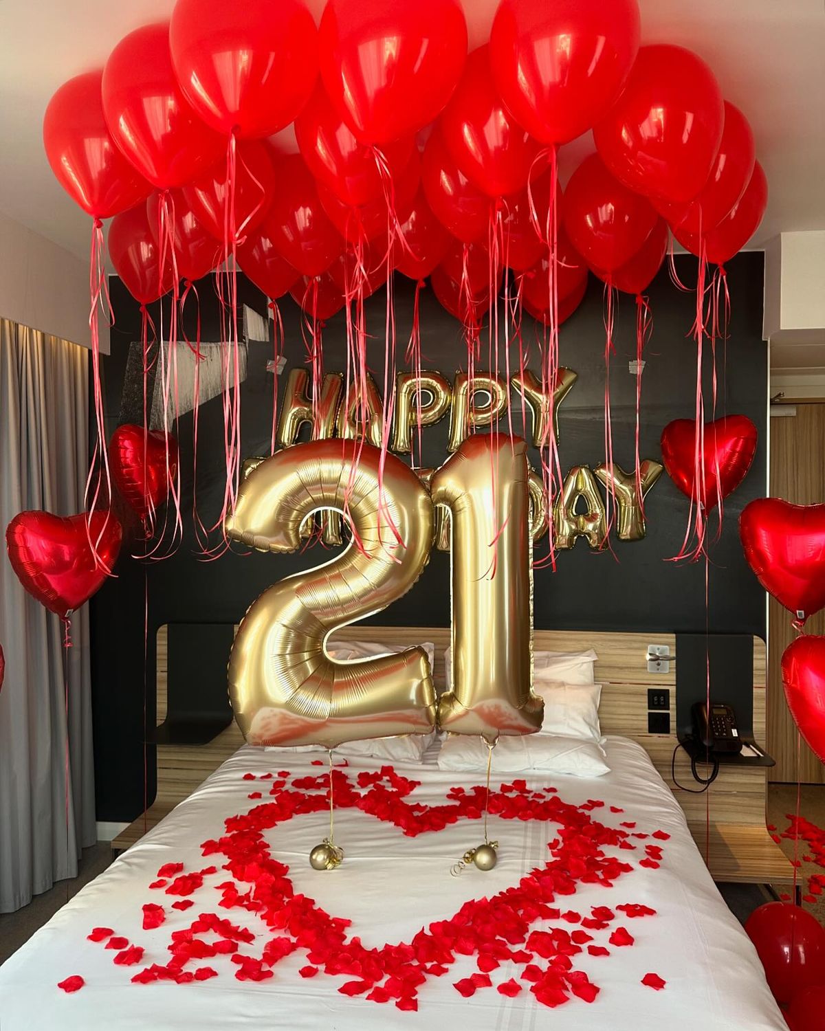 Decorated bedroom with red balloons, heart-shaped decorations, and a gold 'Happy 21st' balloon.