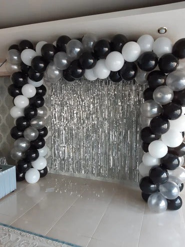 Balloon arch with black, white, and silver balloons in front of a silver curtain.