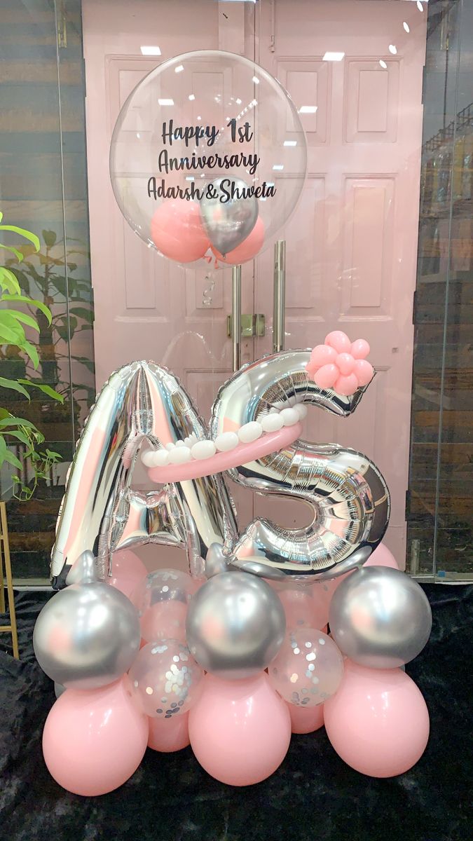 Decorative balloon setup with 'Happy 1st Anniversary' message and initials 'AS' in a pink and silver theme.