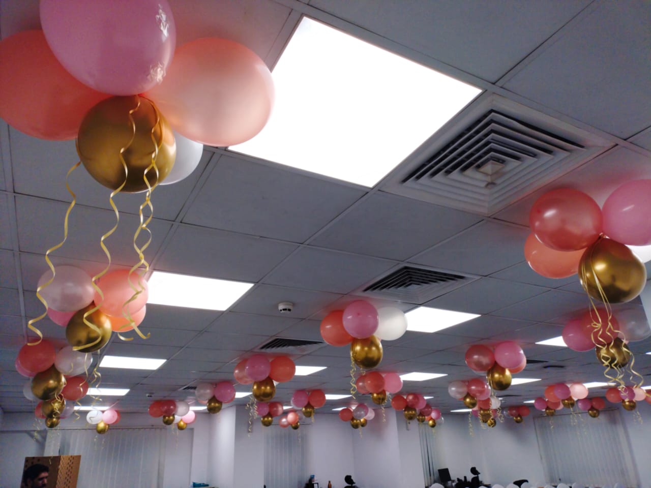 Decorative balloons in pink, gold, and red hanging from the ceiling in a room.