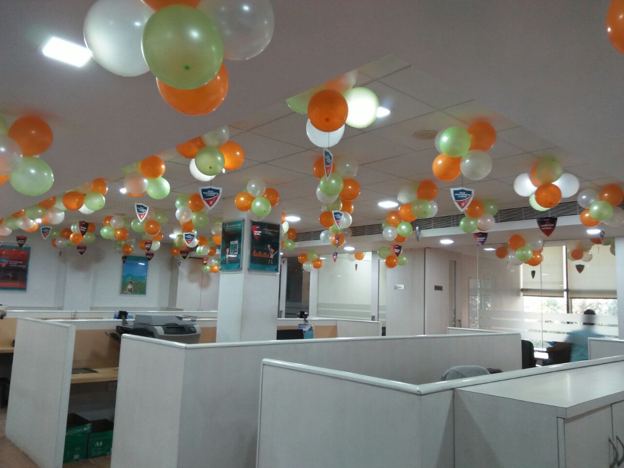 Decorative balloons in orange, green, and white hanging from the ceiling in an office setting.