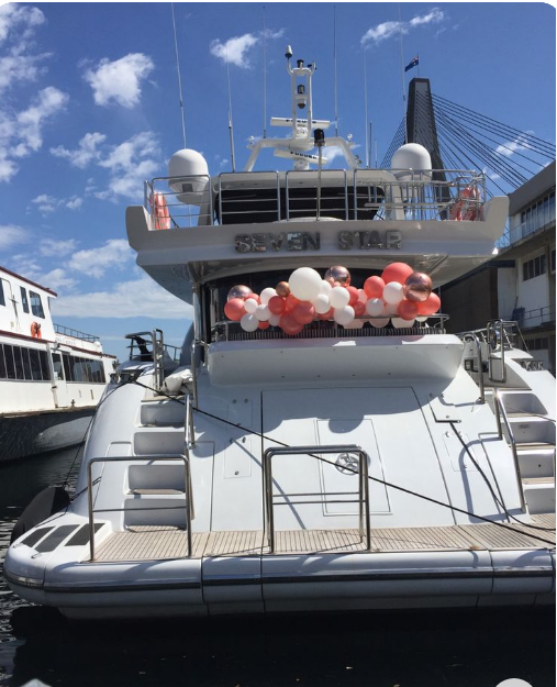 White yacht with balloons docked at a harbor with a clear blue sky.