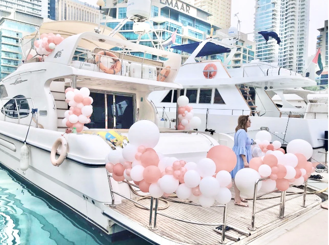 Yacht with pink and white balloon decorations on a city waterfront.