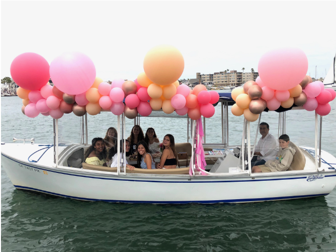 Boat with pink and orange balloons on a body of water with buildings in the background