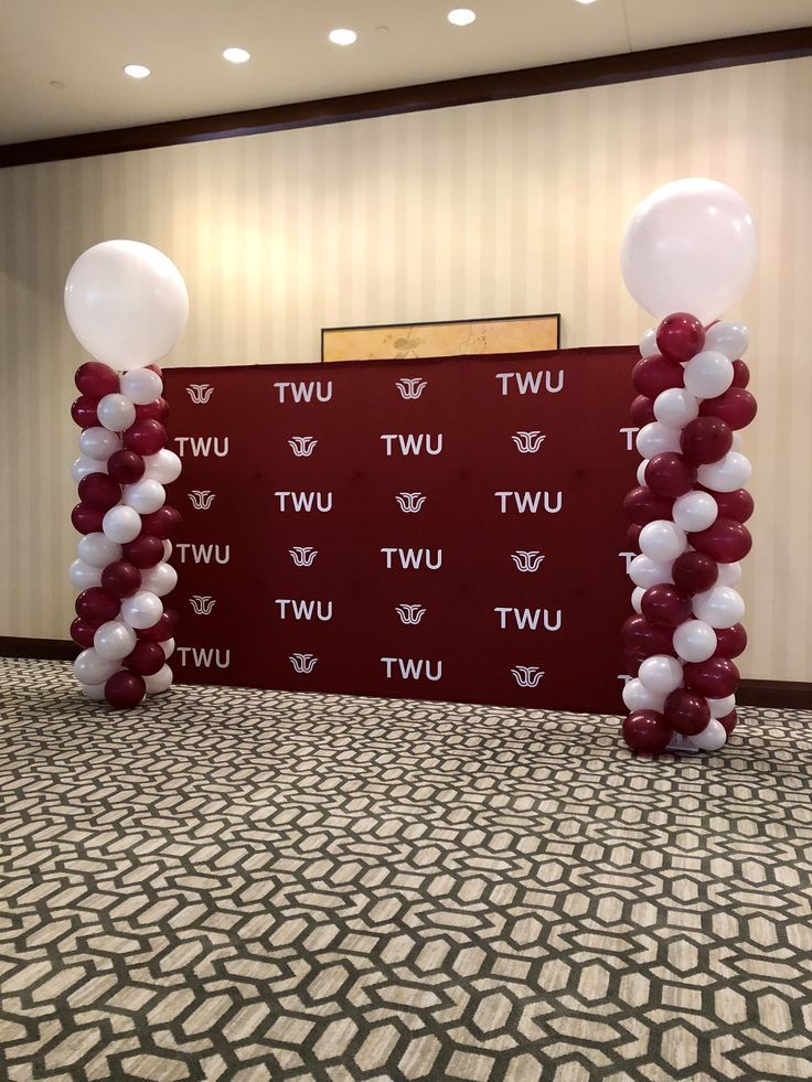 Step and repeat banner with TWU logo flanked by balloon columns in a room.