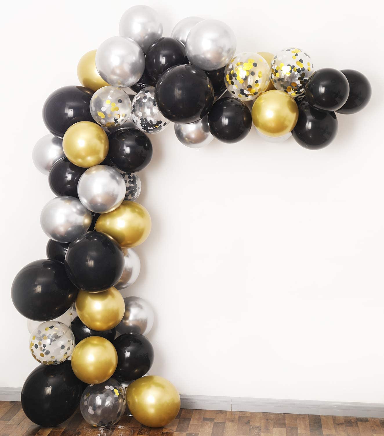 Balloon arch with black, gold, and silver balloons against a white wall.