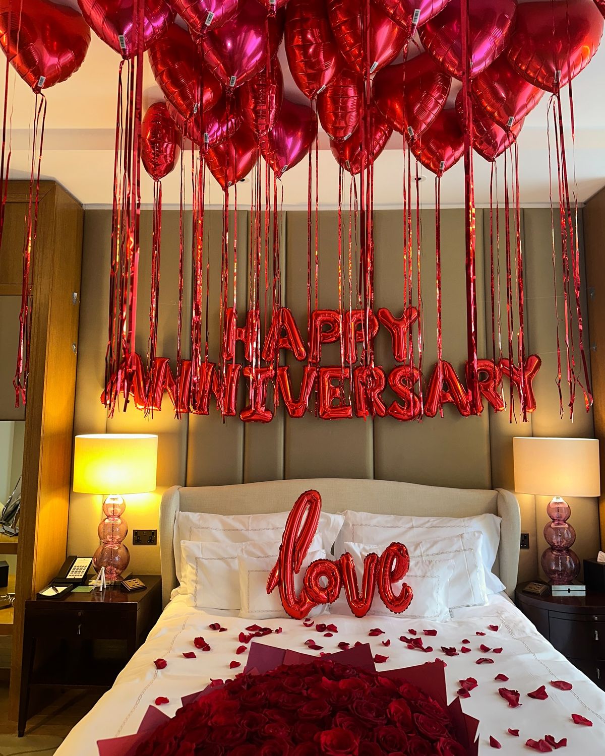 Decorated bedroom with heart-shaped balloons spelling 'Happy Anniversary' and 'Love'.