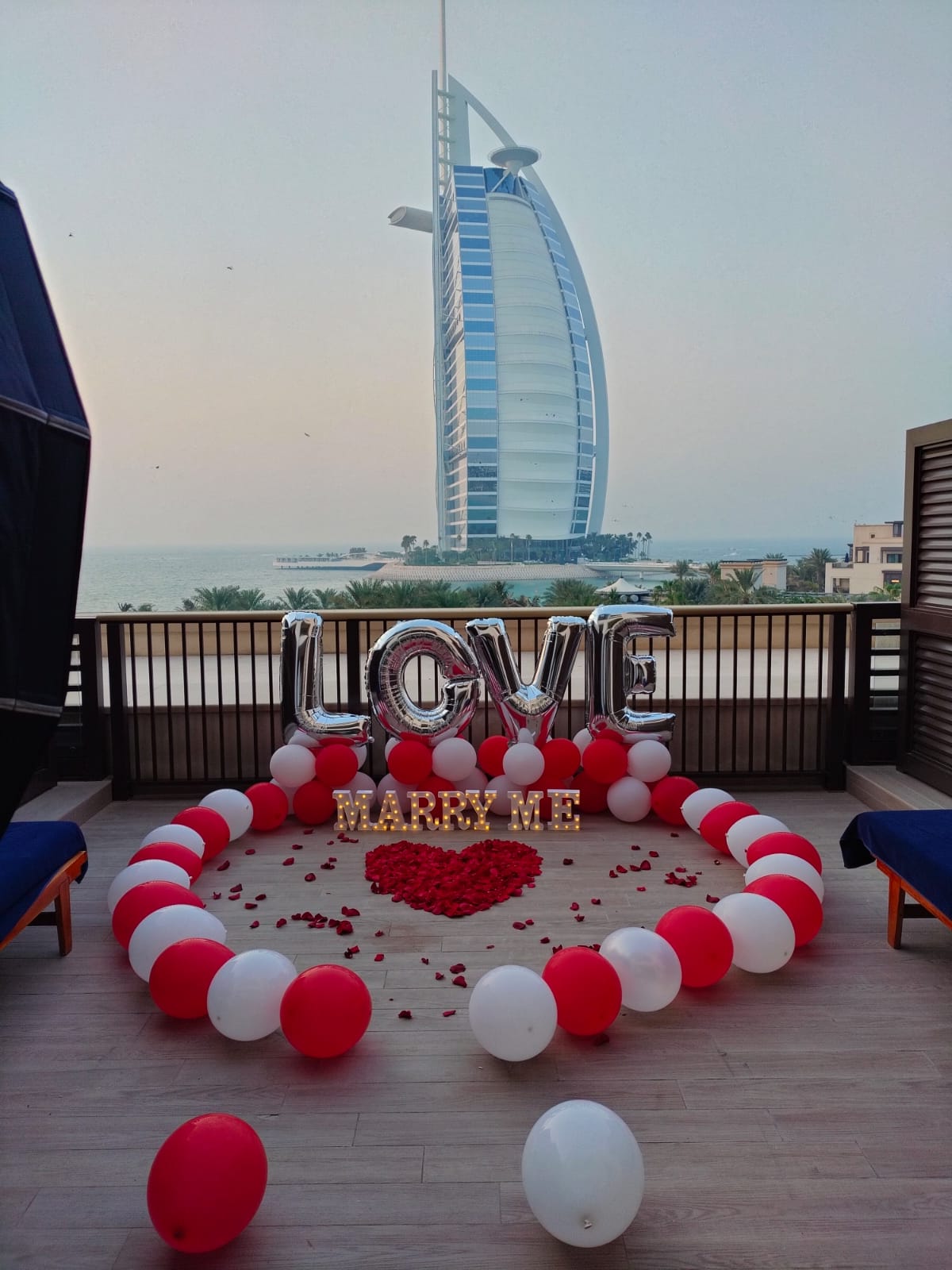 Balloon arrangement with 'LOVE' and 'MARRY ME' text in front of the Burj Al Arab hotel.