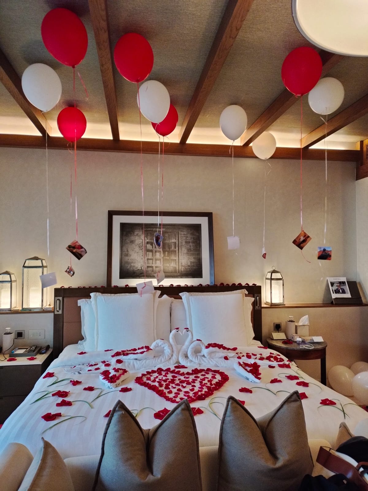 Decorative bedroom with red and white balloons, heart-shaped rose petals, and a framed picture on the wall.