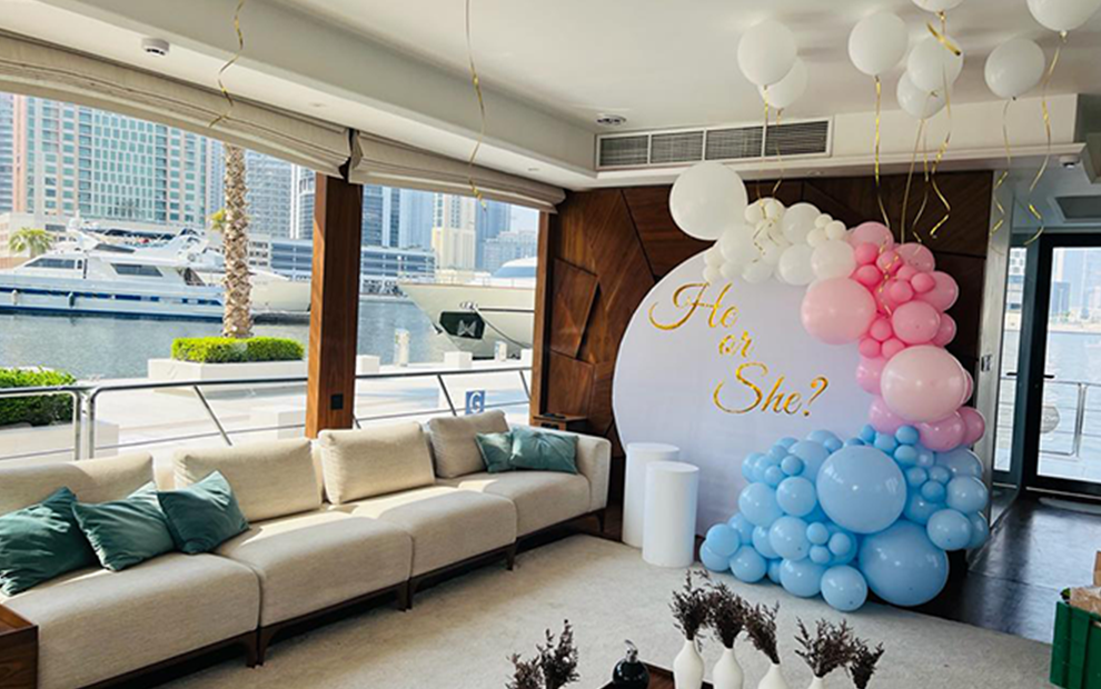 Decorated room with balloons and 'He or She?' question, waterfront view.